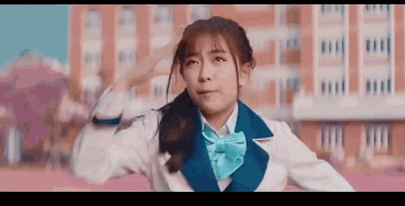 a young woman in a school uniform is saluting in front of a building .