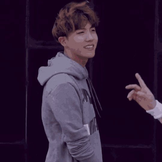 a young man in a gray hoodie is smiling and pointing at another person .
