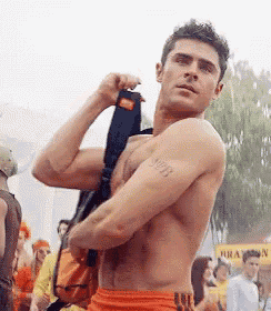 a shirtless man is holding a backpack over his shoulder while standing in front of a crowd .