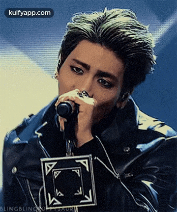 a man is singing into a microphone while wearing a black leather jacket .