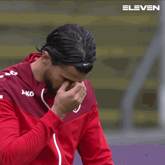a man wearing a headband and a jako jacket wipes his nose