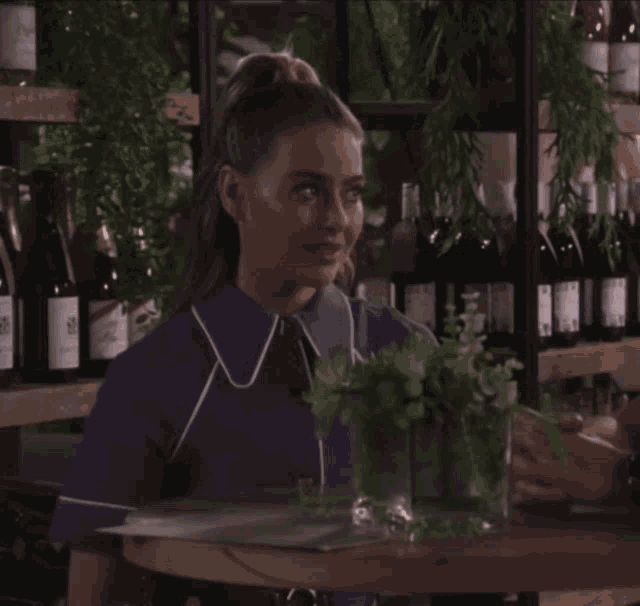 a woman in a purple shirt stands in front of a shelf of wine