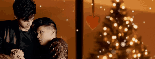 two men hugging in front of a christmas tree with lights