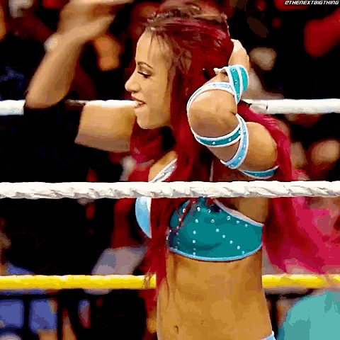 a woman with red hair is standing in a wrestling ring holding her hair .
