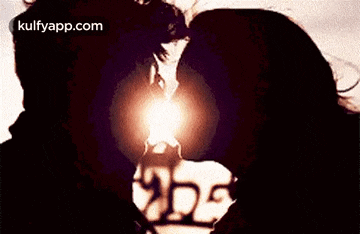 a man and a woman are kissing in front of a heart shaped light .