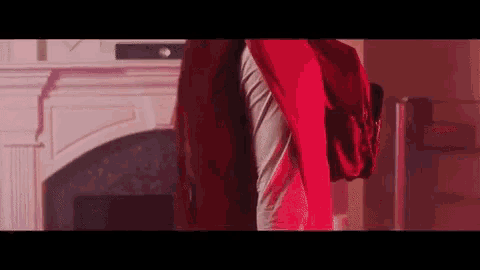 a man in a red shirt is standing in front of a fireplace in a living room .