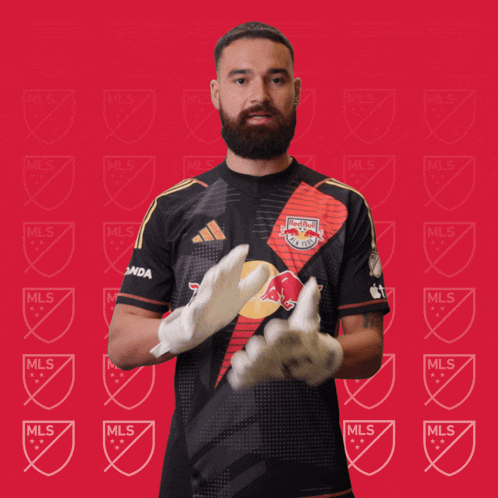 a man wearing a red bull jersey and gloves stands in front of a red background with mls logos