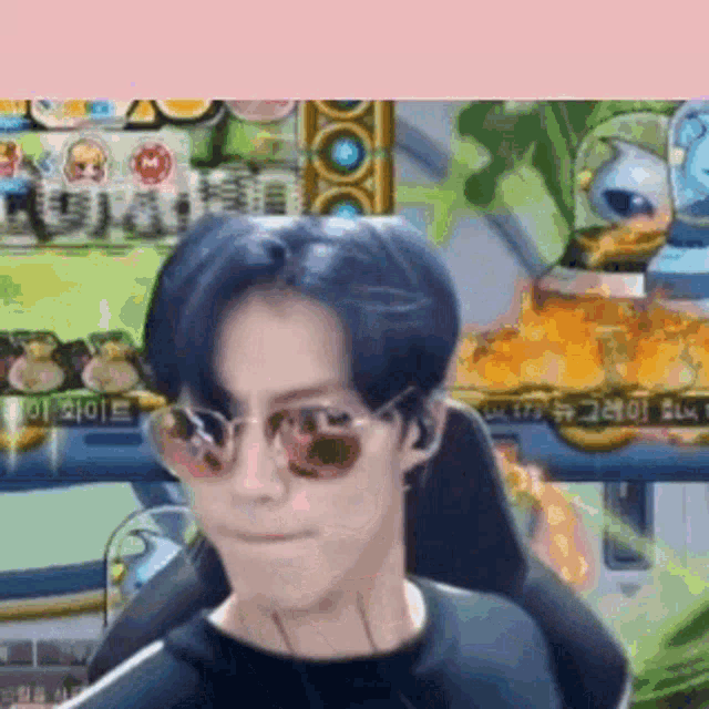 a man wearing sunglasses and a black shirt is sitting in front of a video game screen .