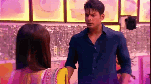 a man and a woman are standing next to each other in a room . the man is wearing a blue shirt .
