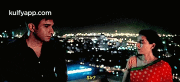a man and a woman are standing next to each other in front of a city skyline at night .