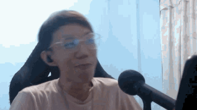 a man wearing glasses is sitting in front of a microphone and making a funny face .