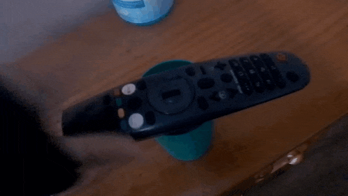 a remote control is sitting on a table next to a green cup
