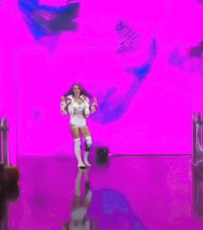 a woman in a white jacket and white shorts is dancing on a stage