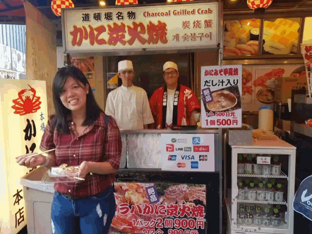 a woman is standing in front of a charcoal grilled crab stand
