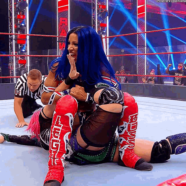 a woman with blue hair is sitting on another woman in a wrestling match