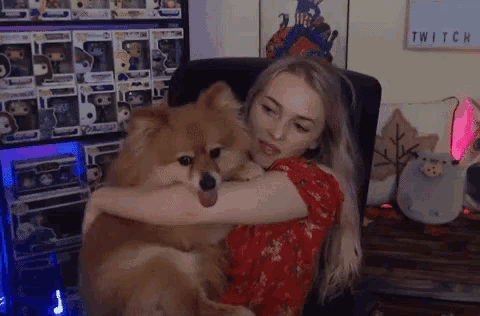 a woman in a red dress is hugging a small brown dog