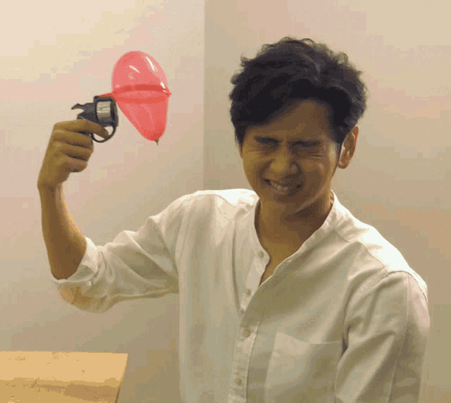 a man in a white shirt is holding a toy gun with a pink balloon in it