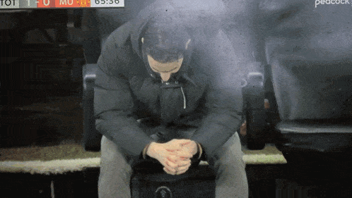 a man sits in a chair with his head down in front of a peacock tv screen