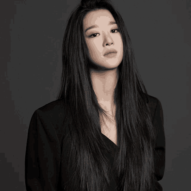 a woman with long black hair wearing a black jacket looks at the camera