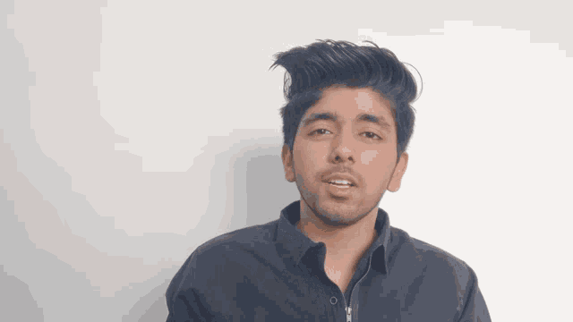 a young man with a beard wearing a blue shirt looks at the camera