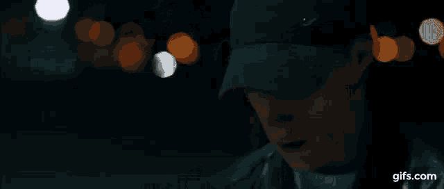a man wearing a hat and a leather jacket is sitting down in the dark .