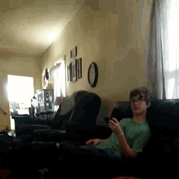 a boy in a green shirt is sitting on a couch looking at a cell phone