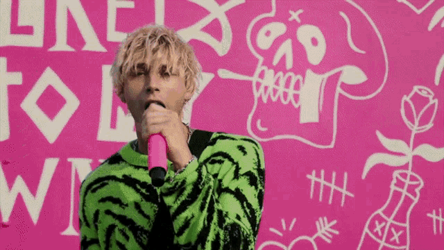 a man singing into a pink microphone in front of a pink wall that says " one to one " on it