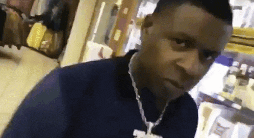 a man wearing a blue shirt and a necklace is standing in a store looking at the camera .