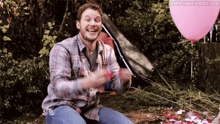a man in a plaid shirt is holding a pink balloon while sitting in front of a tent .