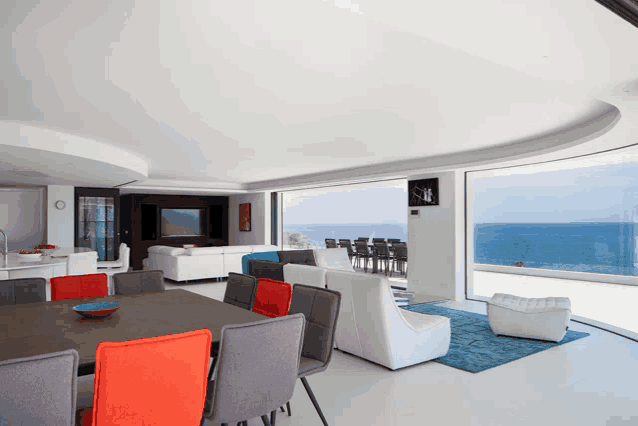 a living room with a dining table and chairs and a large window overlooking the ocean