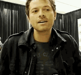 a man wearing a black jacket and a black shirt is standing in a room .