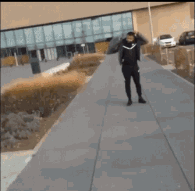 a man is walking down a sidewalk with his hands on his head