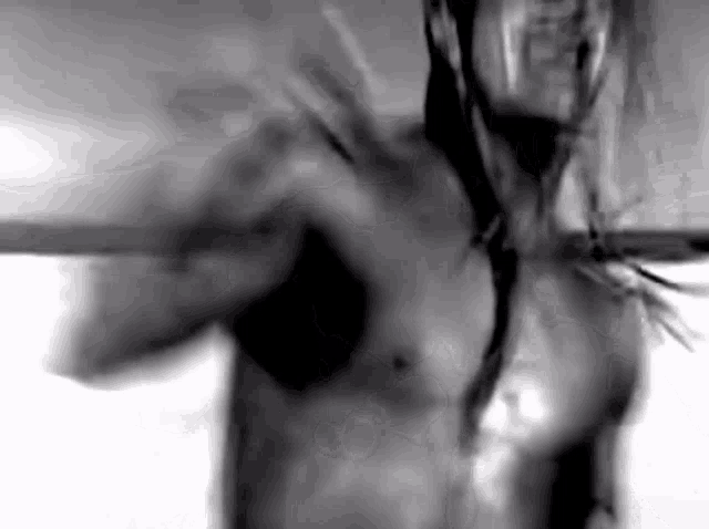 a black and white photo of a shirtless man with long hair holding a sword .