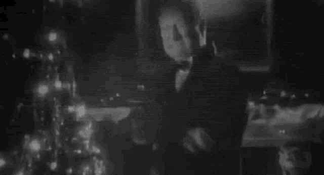 a black and white photo of a man in a tuxedo standing in a dark room .