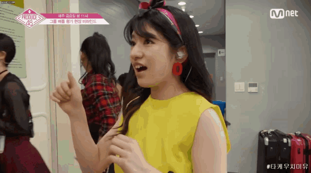 a girl wearing a yellow top and pink earrings is giving a thumbs up