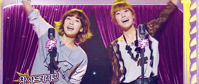 two women standing in front of microphones with a purple curtain behind them and a sign that says ' a ' on it
