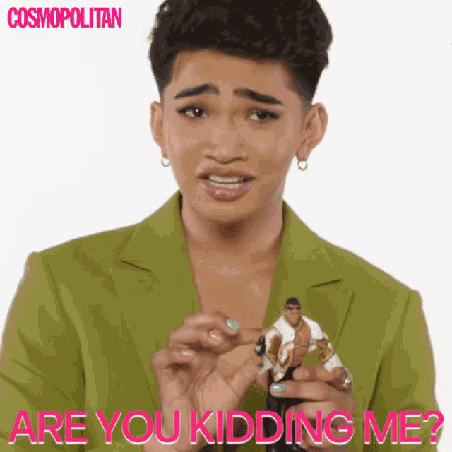 a man in a green jacket is holding a barbie doll and asking if he is kidding me