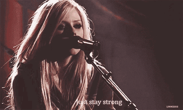 a blonde woman singing into a microphone with the words just stay strong below her