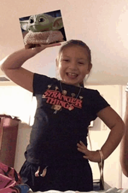 a girl wearing a black shirt that says stranger things holds up a stuffed animal