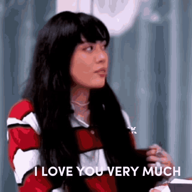 a woman with long black hair is sitting at a table with a cup of coffee and says i love you very much .