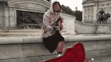 a man is playing a guitar while sitting on a red guitar case .