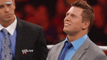 a man in a suit and tie stands next to a man in a suit and tie with a wwe live logo on the bottom