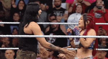 two women are shaking hands in a wrestling ring with a crowd behind them and the letters w on the bottom