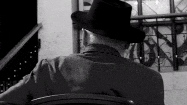 a man wearing a hat sits in a chair with his back to the camera