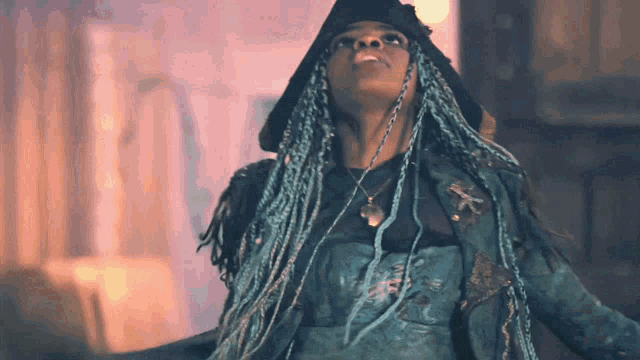 a woman with blue dreadlocks is wearing a black hat and a blue jacket
