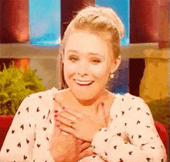 a woman in a polka dot shirt is smiling and holding her hands to her chest .