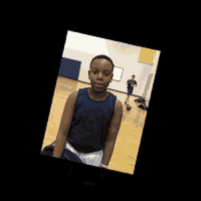 a young boy in a blue tank top and white shorts is standing in a gym