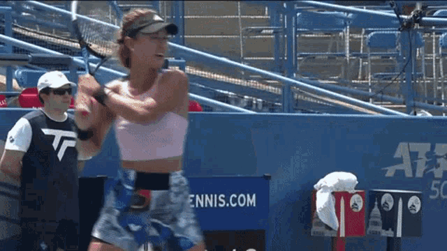 a woman swings a tennis racquet in front of a tennis.com sign