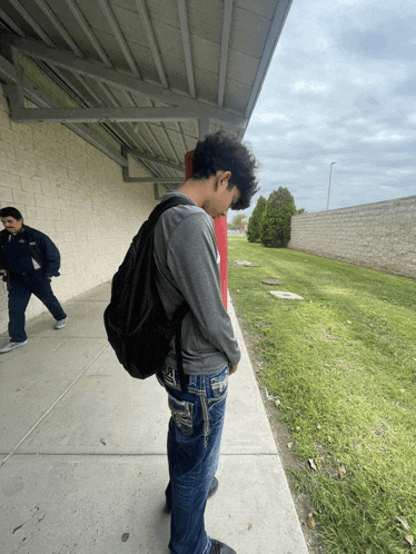 a young man with a backpack is standing on a sidewalk