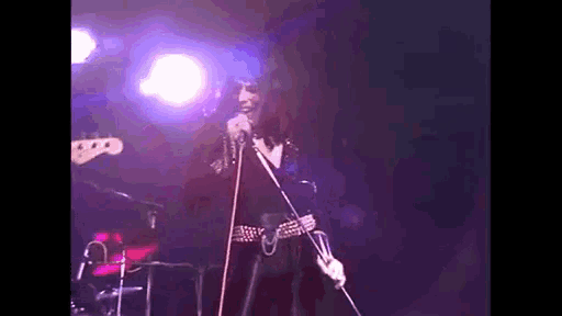 a woman is singing into a microphone on a stage in front of a drum set .